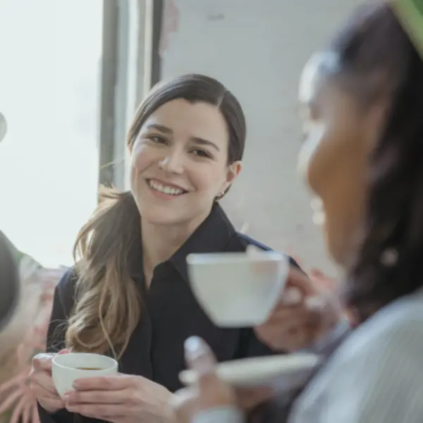 endometriosis-management-macleod-rosanna-social-confidence Two women smiling and talking over coffee, representing the social confidence and community participation supported by evidence-based endometriosis management at Monty Pelvic Physio.