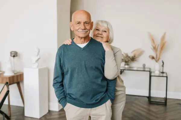 An older man smiling with a woman standing behind him with her hands on his shoulders, representing supportive mens pelvic health care at Monty Pelvic Physio near Greensborough.