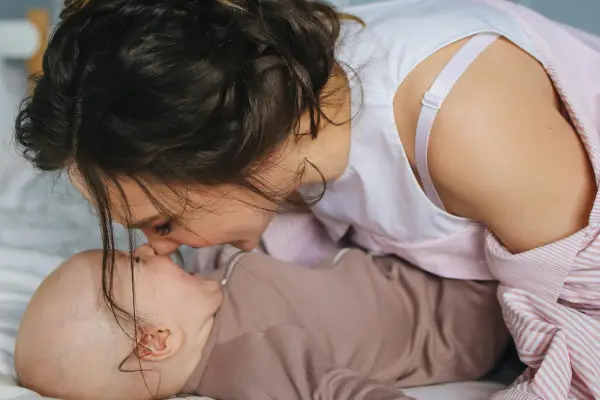 A mother leaning down to gently touch foreheads with her baby on a bed, representing tender postpartum bonding and recovery support at Monty Pelvic Physio in Eltham.